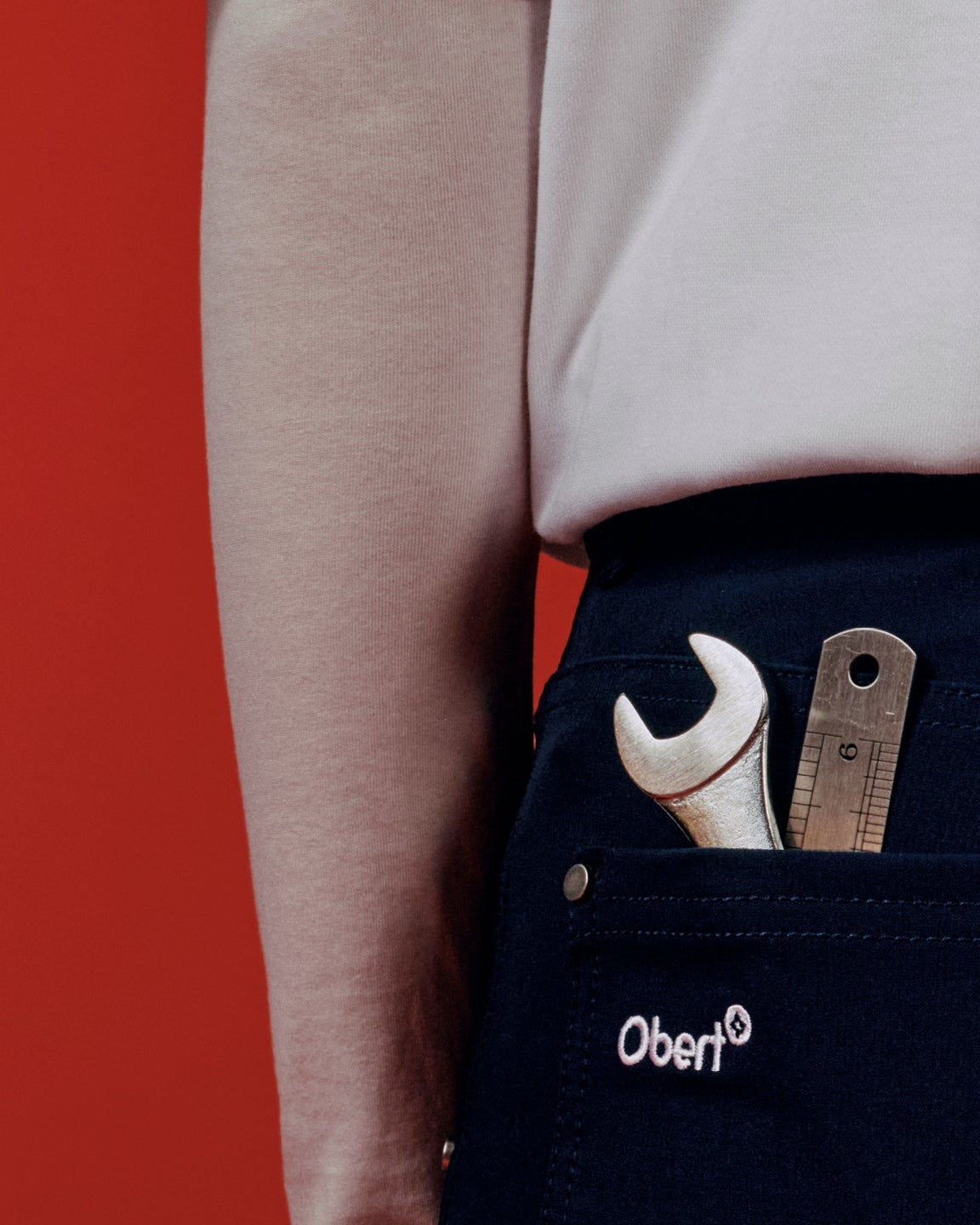 Person wearing navy pants with a tool pocket featuring a wrench and screwdriver, against a red background.