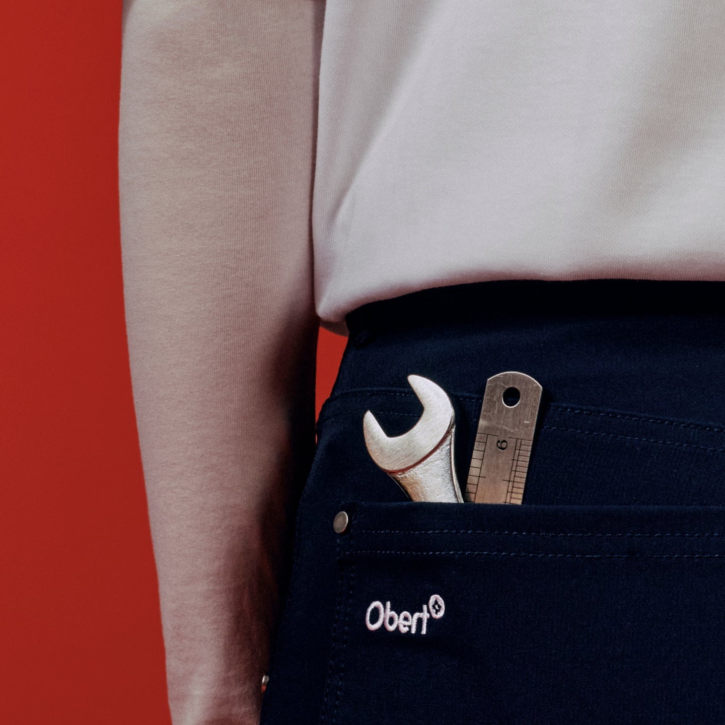 Person wearing navy pants with a tool pocket featuring a wrench and screwdriver, against a red background.