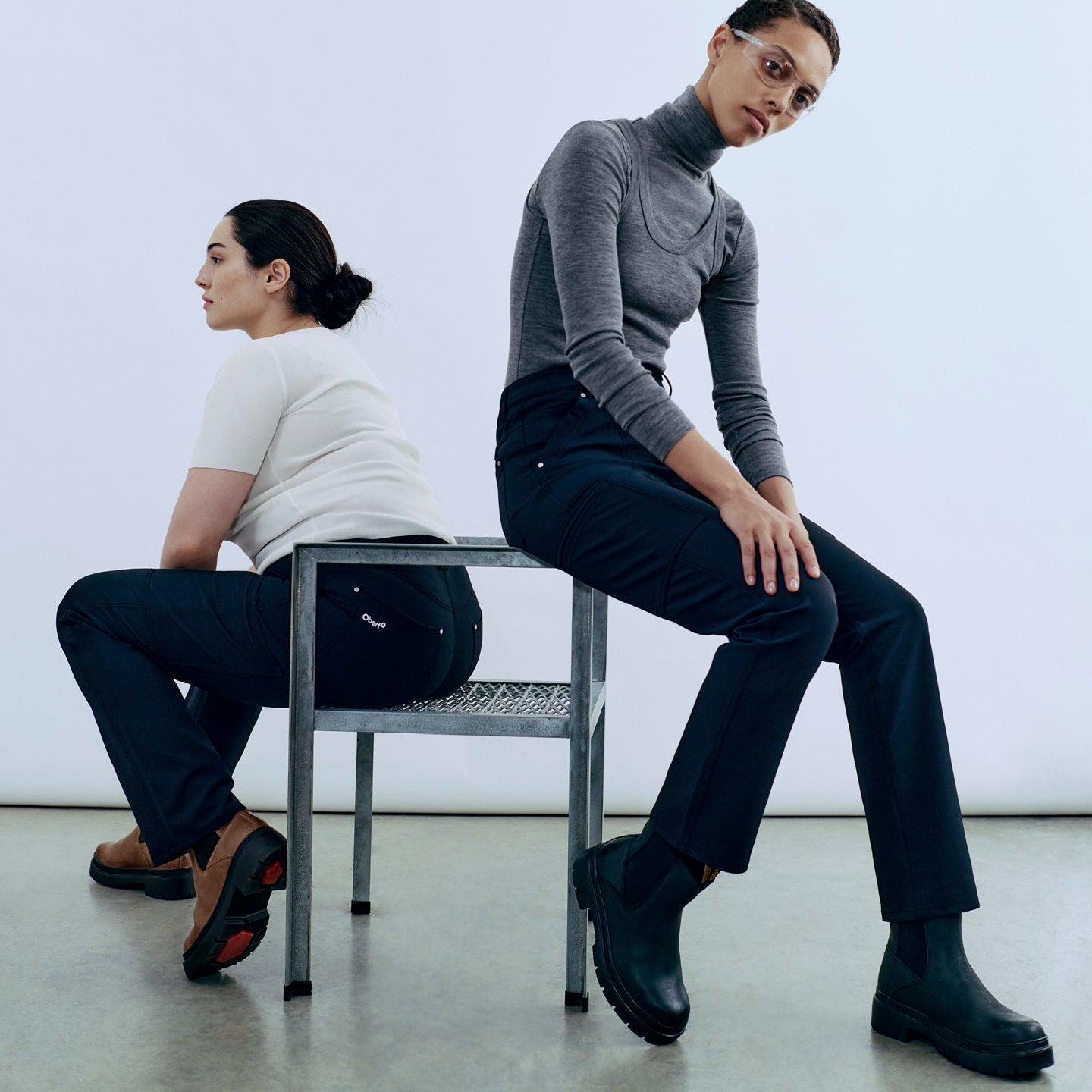 Two people sitting on a chair in a minimalistic room.