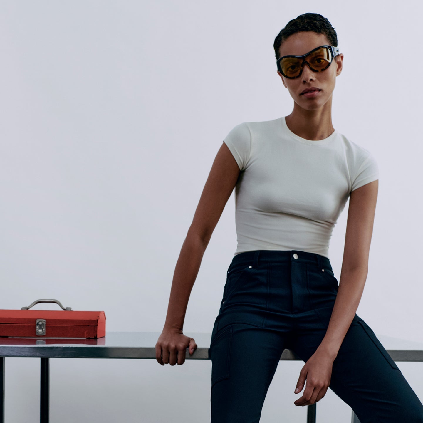 Woman sitting on a table with a red toolbox next to her against a plain background
